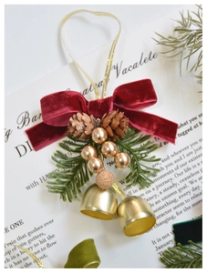 Detail of Christmas bell ornament with red velvet bow, pine cone, and gold bell accent