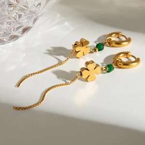 Detail of gold clover earrings with green beads and long tassels by a glass cup