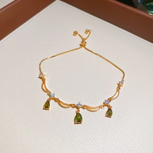 Dettaglio del bracciale placcato oro con pietra a goccia verde e zirconi su pelle