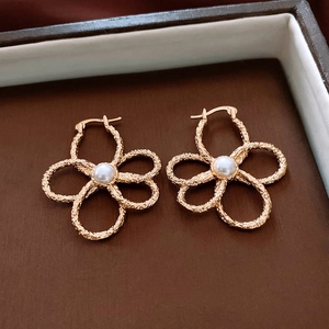 Close-up of golden hollow flower earrings featuring textured petals and a center pearl