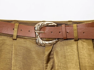 Detail of a brown leather belt with gold irregular metal buckle on olive satin pants