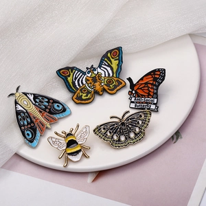 Five creative insect enamel pins including bees and moths on a minimalist white plate