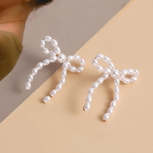 Detail of handcrafted cream pearl bow earrings with golden metal framing for women