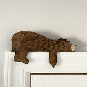 Detail view of a hand-carved brown wooden bear topper resting on a white door frame