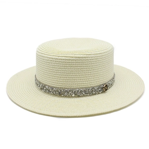 Detail view of woven straw hat with silver rhinestone band and golden M emblem