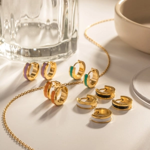 Detail of colorful enamel hoop earrings and gold necklace on white ceramic surface
