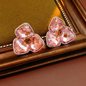 Close-up of diamond-studded floral stud earrings with pink faceted crystals on a wooden frame