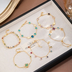 Detail of assorted gold bracelets with colorful stones and clover charms in a display tray
