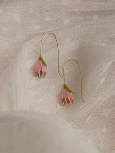 Detailed macro of pink tulip enamel drop earrings on elegant white lace background