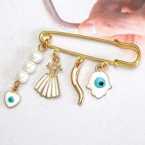 Detail of gold safety pin brooch with Evil Eye Hamsa and heart charms with pearls
