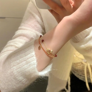 Détail d'un bracelet double couche plaqué or 18 carats avec perle rouge et pendentif cheval à bascule