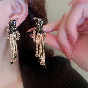 Boucles d'oreilles longues dorées avec strass noirs et champagne portées et tenues à la main