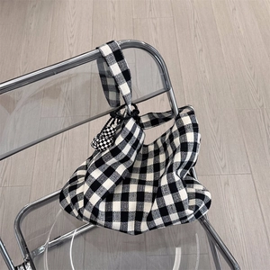 Detail of checkered canvas tote bag with matching ball charm on a clear chair