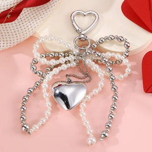 Silver heart pendant keychain with white pearl bow and metallic accents for bags