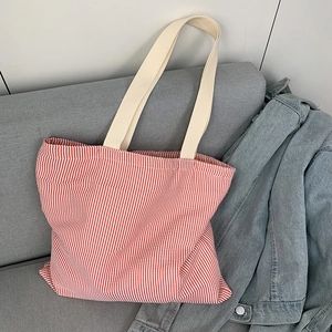 Detail of red and white striped canvas tote bag on a grey sofa with beige shoulder straps
