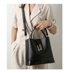 Detail of black pebbled and crocodile leather tote with gold metal buckle on female model
