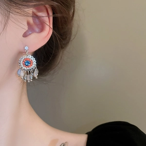 Detail view of retro flower earrings with blue crystal and beaded tassels on a model