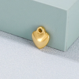 Polished gold heart pendant with round bail displayed on a minimalist geometric background
