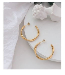 Detail of twisted double-layer gold hoop earrings on a minimalist white display tray