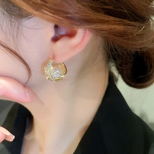 Gros plan d'une boucle d'oreille dorée géométrique avec cristaux pavés et perle blanche