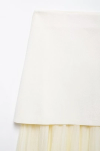 Close-up of pleated beige knit fabric stitched with champagne tulle mesh hemline detail