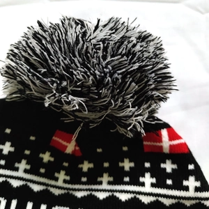 Close-up of a black knit Christmas beanie showing the mixed pompom and jacquard patterns