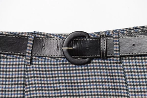 Detail of plaid midi skirt featuring a black leather belt with a circular buckle