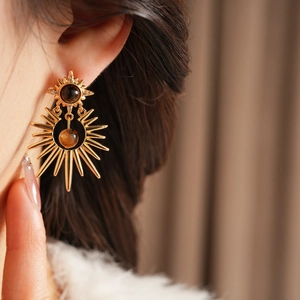 Close-up of gold starburst earrings with brown stones and zircon on female model