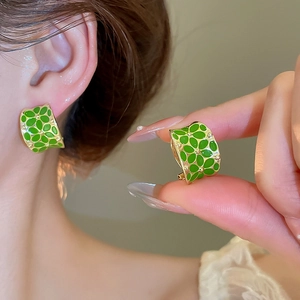 Detail showing hand holding green enamel flower earrings with gold finish and C-shape design