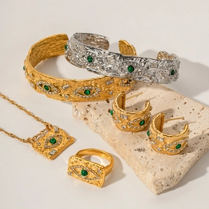 Lava style gold and silver Evil Eye jewelry set with green stones on a stone pedestal