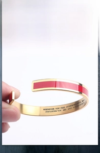 Close-up of golden stainless steel cuff bracelet with red enamel and engraved quote for daughter