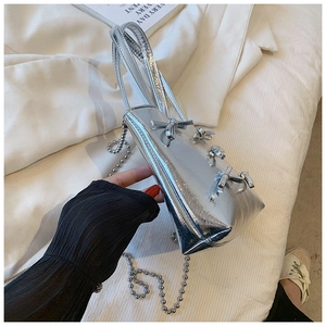Detail of silver metallic triangle handbag with knot accents and a slim chain strap