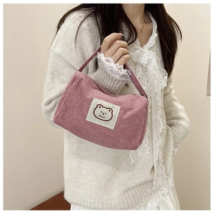 Close-up of pink corduroy handbag with cartoon bear patch held by a model