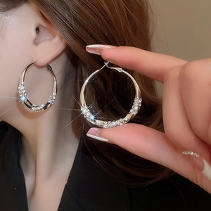 Detailed view of silver hoop earrings with shimmering rhinestones worn by a model