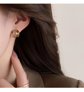 Close-up of wide C-shaped earrings with gold metal and khaki enamel on model