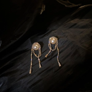 Detail of long gold tassel earrings with pearls and rhinestones on black silk fabric