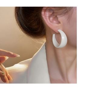 Close-up of a white chunky acrylic C-shaped hoop earring worn on a model's ear
