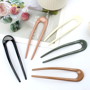 Five assorted resin U-shaped hair pins for bun styling in neutral tones on a clean white desk