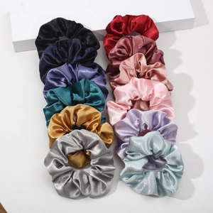Detailed view of satin scrunchies in 12 vibrant colors on a minimalist white stand