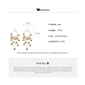 Détail de boucles d'oreilles dorées à pompons avec disques texturés et mesure de 11,5 cm