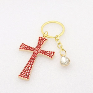 Close-up of golden cross keychain featuring red rhinestones and clear teardrop gem
