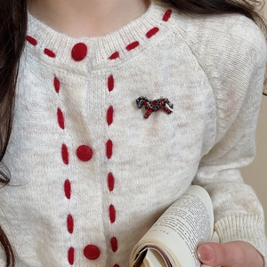 Détail d'une broche cheval en émail rouge avec cristaux sur un pull en maille élégant
