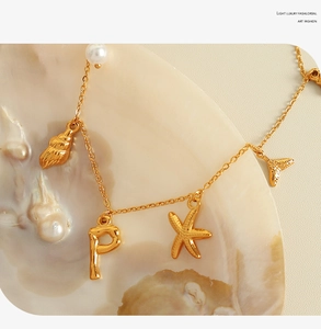 Detailed macro view of 18K gold letter P pendant with starfish, conch and pearl