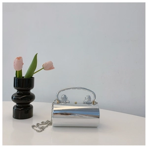 Silver cylindrical mirror evening bag with lion head handles and chain on a table