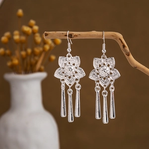 Detail of silver ethnic drop earrings with peacock bell fringe hanging on a wood branch