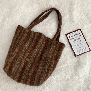 Close-up of brown faux fur tote bag with green stripes and oval metal logo detail