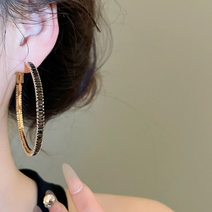 Close-up of large golden hoop earrings with baguette-cut black stones for women