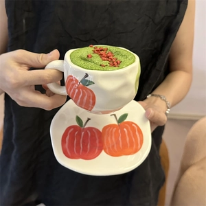 Close-up of hand-painted ceramic apple pattern coffee cup and saucer held by hands