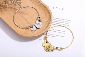 Detail of adjustable wire bracelets with silver and gold engraved charms on a wooden tray