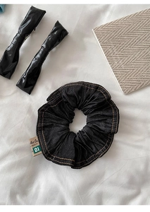 Detail view of black denim scrunchie and glossy hair clip on a soft white cloth background
